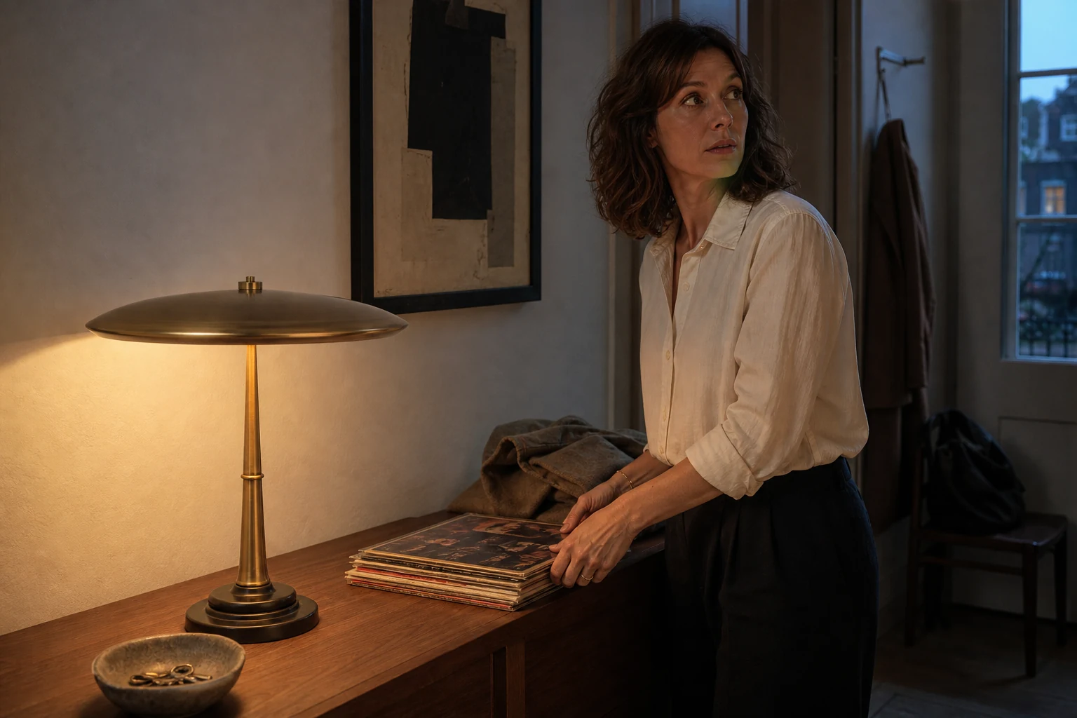 Woman preparing an entry console beside the illuminated Halo Rib sculptural brass table lamp at blue hour