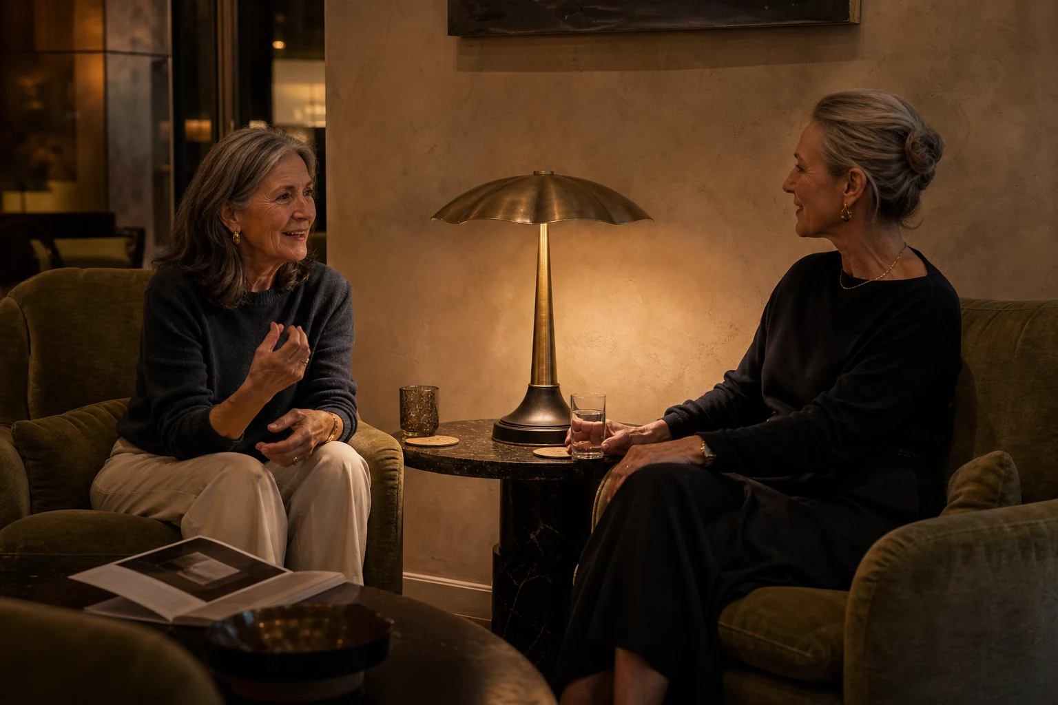 Two older friends in conversation beside the illuminated Petal Disc brass lounge table lamp